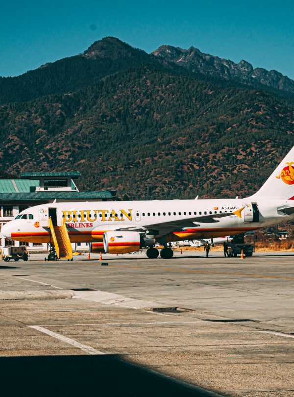 A Bhutan Airlines aircraft parked at Paro Airport with scenic mountain backdrop.