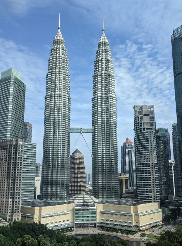 Panoramic view of the iconic Petronas Towers in Kuala Lumpur against a blue sky.
