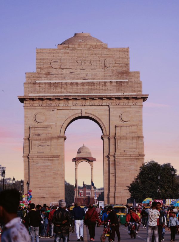 A bustling scene at India Gate with a vibrant crowd under a colorful sunset sky.