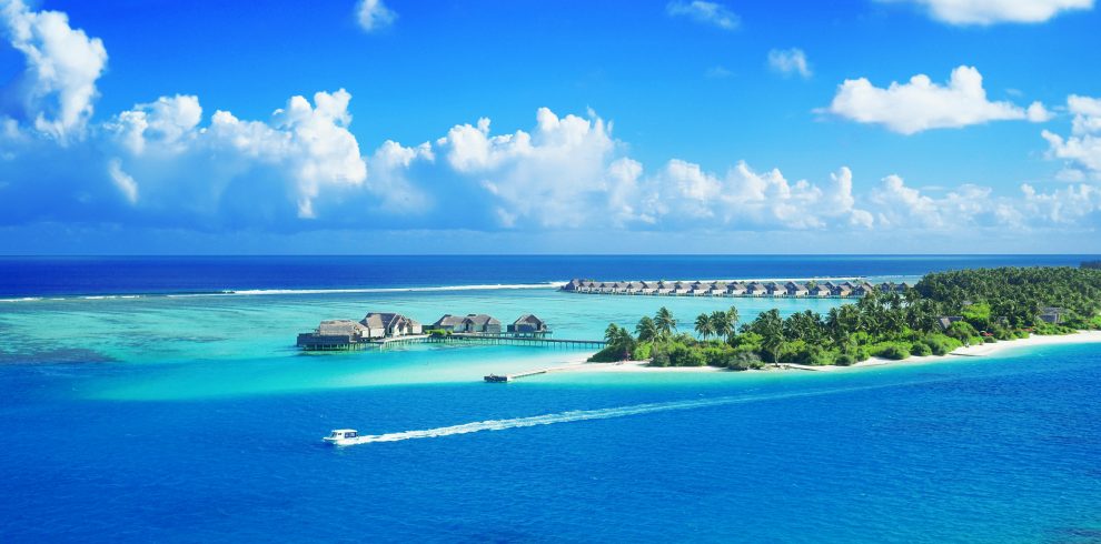 Crystal clear waters surround a luxurious Maldives resort under a bright blue sky.